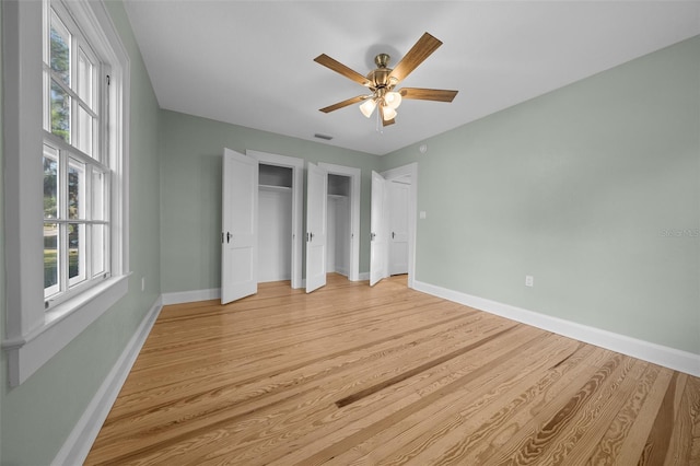 unfurnished bedroom featuring baseboards, light wood-type flooring, two closets, and ceiling fan