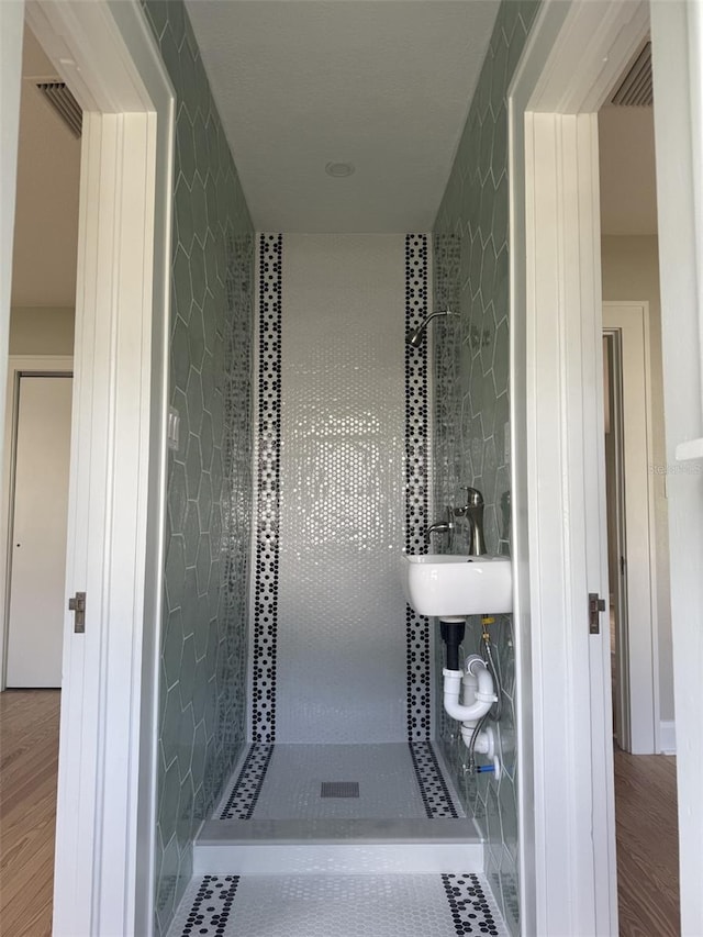 bathroom with a tile shower, a sink, and wood finished floors