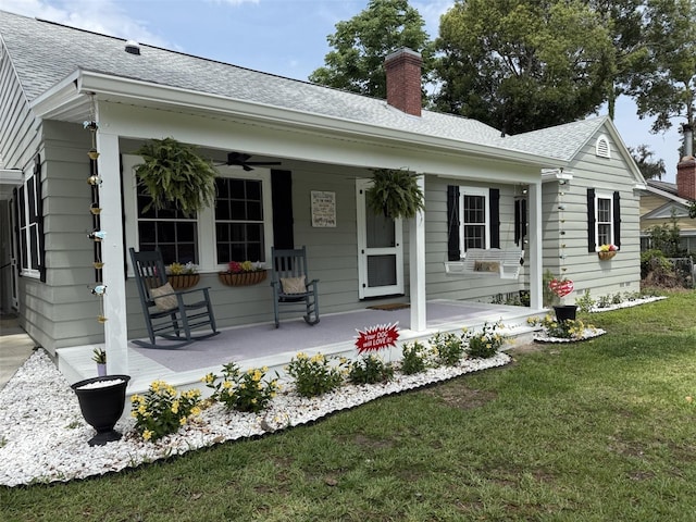 back of property with covered porch, a yard, a ceiling fan, a chimney, and a shingled roof