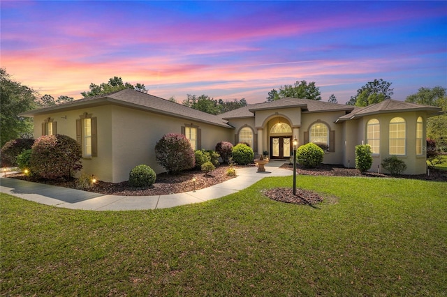 mediterranean / spanish-style home with a front yard, stucco siding, and french doors