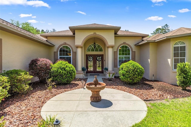 property entrance with roof with shingles, stucco siding, and french doors