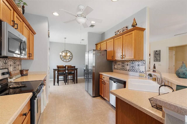 kitchen with light countertops, ceiling fan with notable chandelier, a sink, and stainless steel appliances