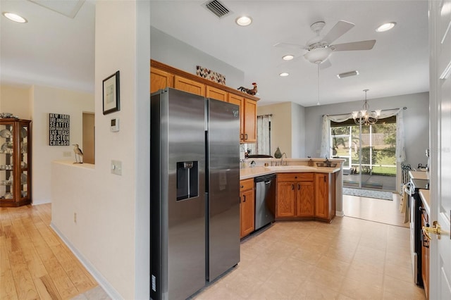 kitchen with visible vents, a peninsula, brown cabinetry, ceiling fan with notable chandelier, and stainless steel appliances