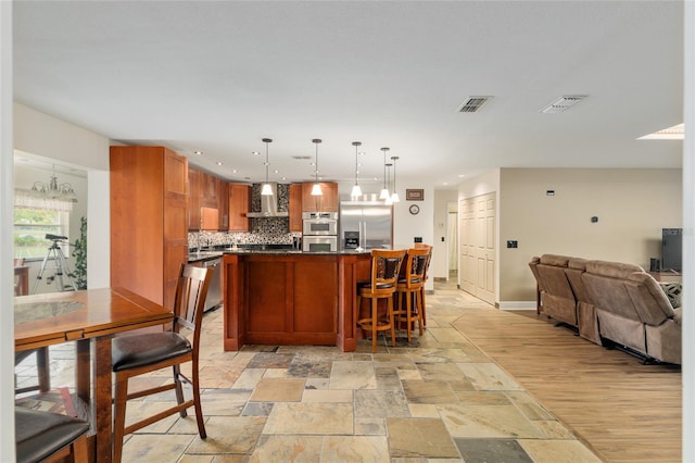 kitchen with open floor plan, appliances with stainless steel finishes, wall chimney range hood, and visible vents