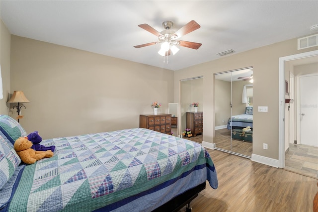 bedroom featuring visible vents, multiple closets, a ceiling fan, and wood finished floors
