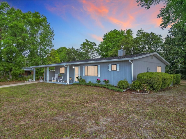 ranch-style house featuring an attached carport, a front yard, driveway, and a chimney