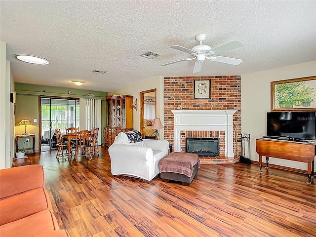 living room featuring a fireplace, a textured ceiling, visible vents, ceiling fan, and wood finished floors