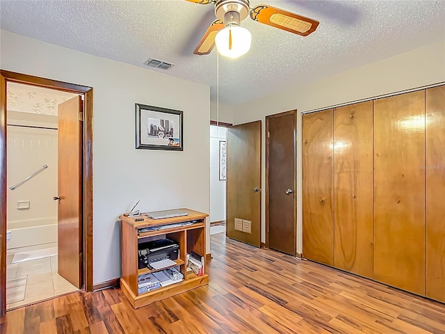 interior space featuring a closet, a textured ceiling, a ceiling fan, visible vents, and wood finished floors