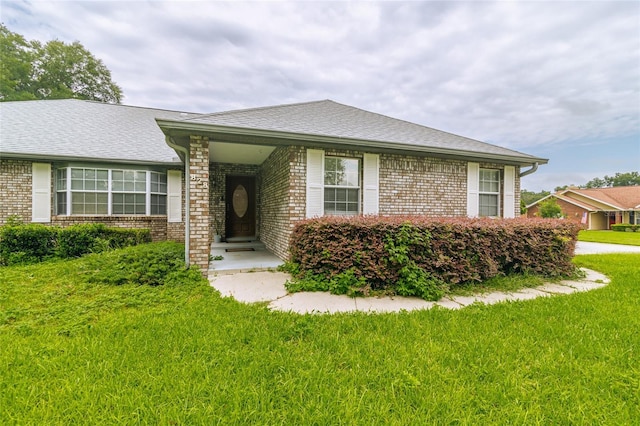 single story home with brick siding, a shingled roof, and a front lawn