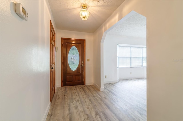 entryway featuring baseboards, a textured ceiling, and light wood-style floors