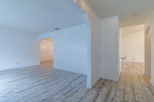 unfurnished room featuring a textured ceiling, visible vents, baseboards, wood finished floors, and arched walkways