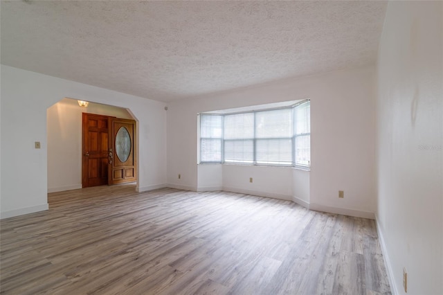 spare room featuring arched walkways, a textured ceiling, baseboards, and wood finished floors