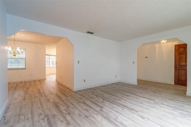 unfurnished room featuring arched walkways, light wood-style floors, a notable chandelier, and visible vents