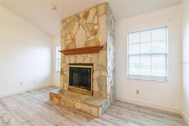 unfurnished living room featuring a stone fireplace, baseboards, lofted ceiling, and wood finished floors