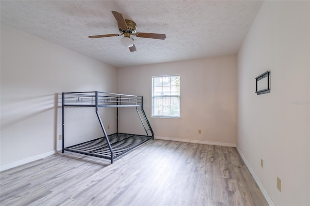 unfurnished bedroom with baseboards, a textured ceiling, wood finished floors, and ceiling fan