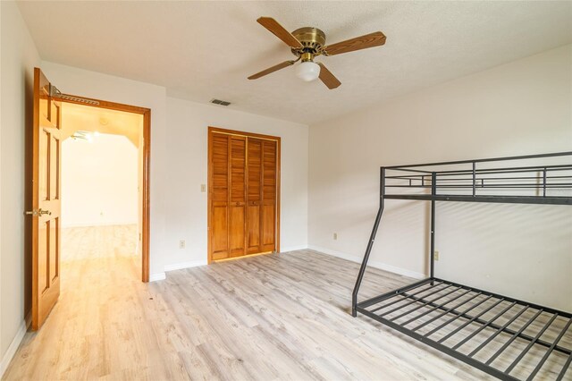 unfurnished bedroom featuring a closet, visible vents, baseboards, wood finished floors, and a ceiling fan