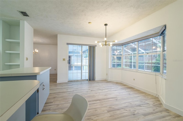 dining area with a textured ceiling, light wood-style flooring, an inviting chandelier, and built in shelves