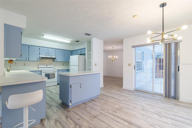 kitchen with a sink, blue cabinets, under cabinet range hood, white appliances, and an inviting chandelier