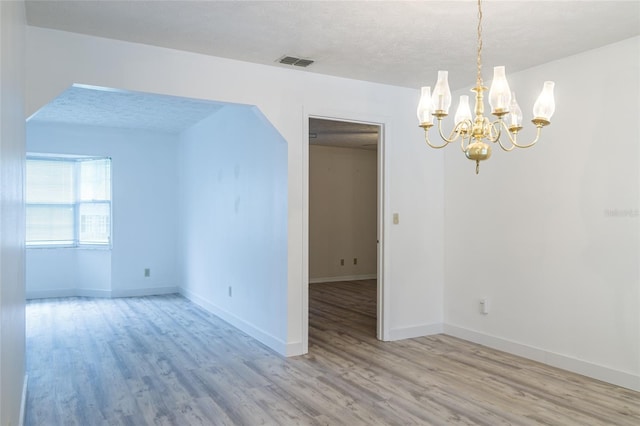 spare room featuring a textured ceiling, visible vents, wood finished floors, and an inviting chandelier