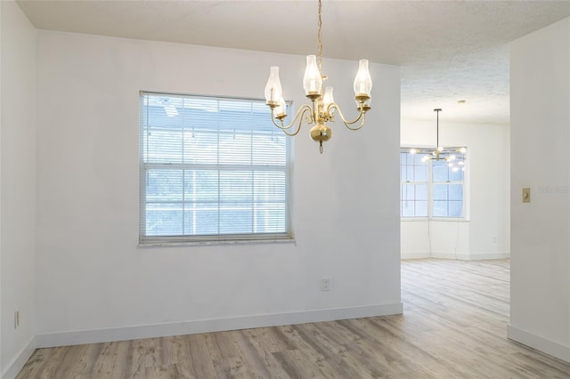 unfurnished room featuring baseboards, a wealth of natural light, wood finished floors, and a chandelier