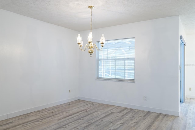unfurnished room featuring baseboards, a notable chandelier, wood finished floors, and a textured ceiling