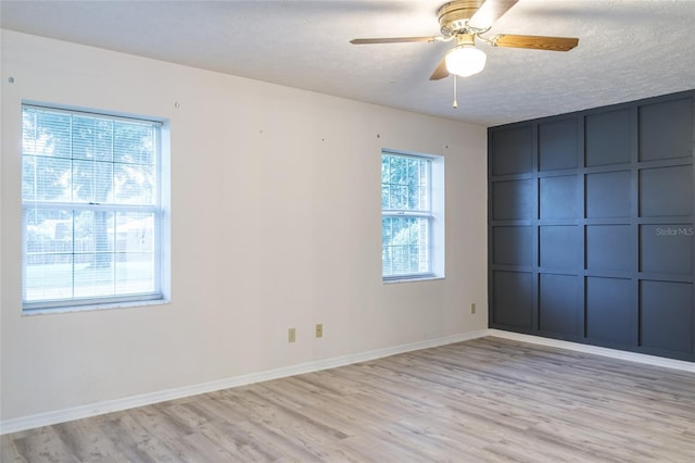 empty room with baseboards, a textured ceiling, light wood-style flooring, and a ceiling fan