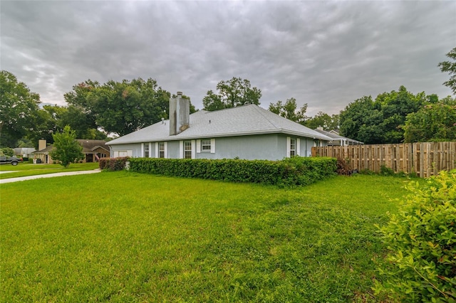 view of property exterior with stucco siding, a chimney, fence, and a yard