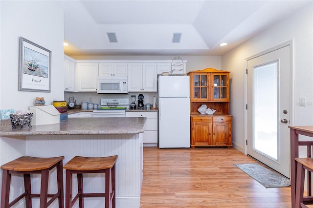 5770 SW 89th Pl, Ocala, FL 34476 - kitchen featuring light wood-style floors, white appliances, a raised ceiling, a kitchen bar, and white cabinets