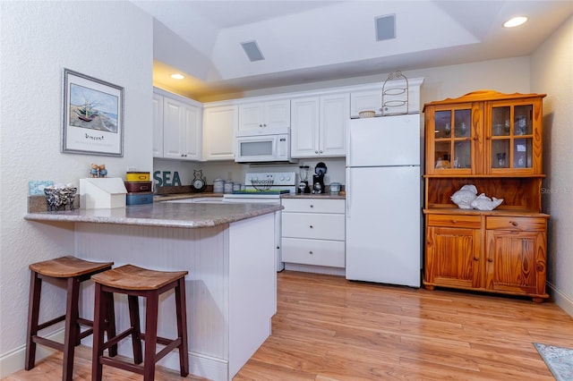 5770 SW 89th Pl, Ocala, FL 34476 - kitchen featuring white cabinets, a tray ceiling, a breakfast bar, white appliances, and a peninsula