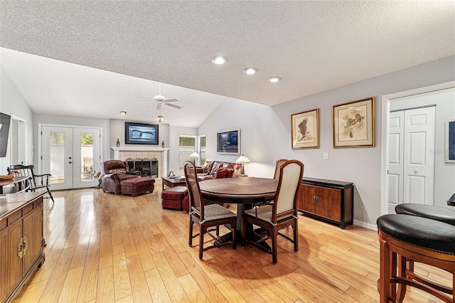 dining room featuring vaulted ceiling, ceiling fan, light wood-type flooring, and a fireplace