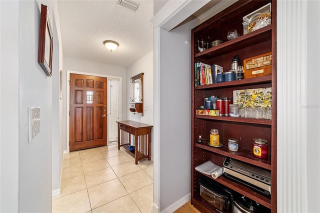 foyer entrance featuring light tile patterned floors, a textured ceiling, baseboards, and visible vents