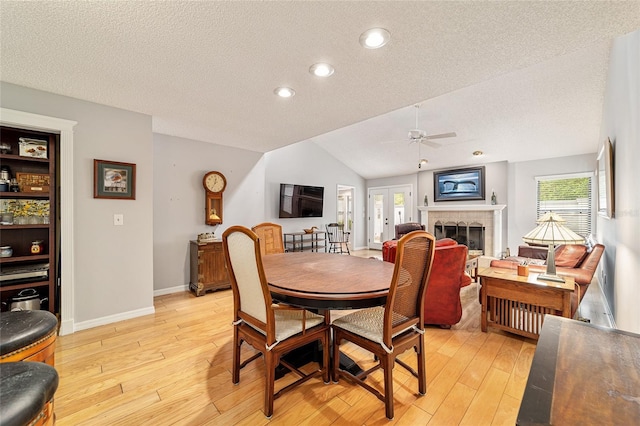 dining area featuring a textured ceiling, light wood-style flooring, a fireplace, a ceiling fan, and vaulted ceiling
