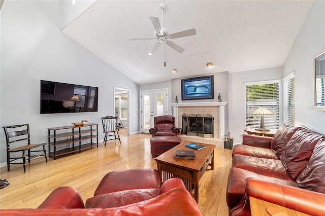 living room with a textured ceiling, a tile fireplace, baseboards, ceiling fan, and wood finished floors