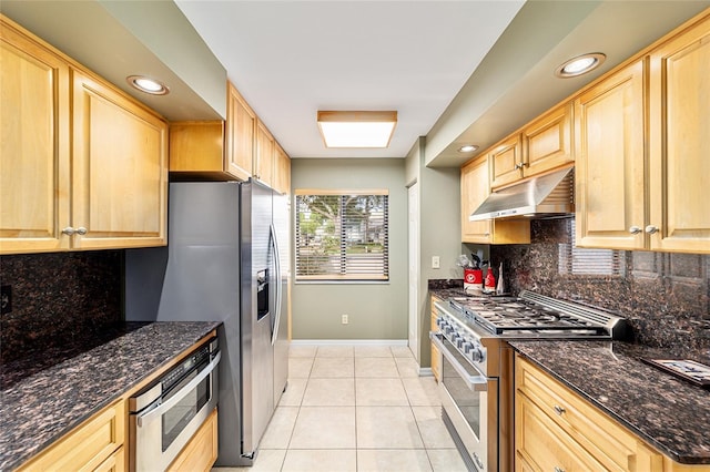 kitchen with light tile patterned floors, under cabinet range hood, baseboards, high end stainless steel range, and light brown cabinets