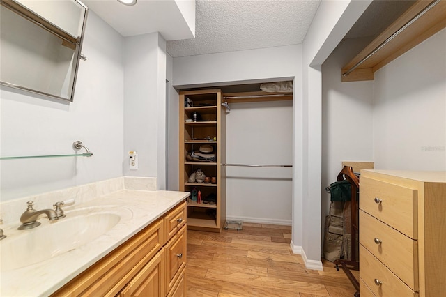bathroom featuring vanity, a walk in closet, a textured ceiling, and wood finished floors