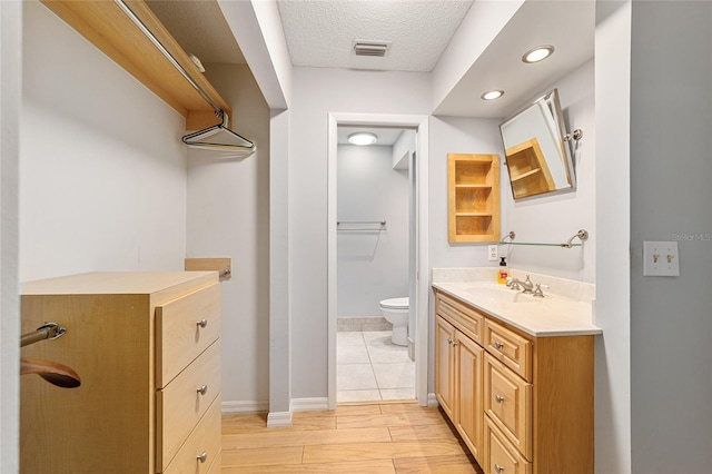 bathroom with vanity, toilet, baseboards, a textured ceiling, and visible vents