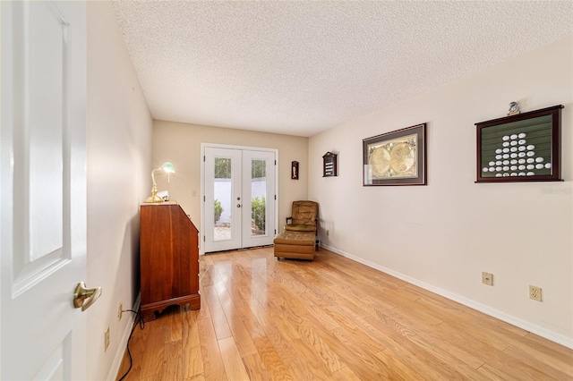 living area featuring french doors, baseboards, light wood finished floors, and a textured ceiling