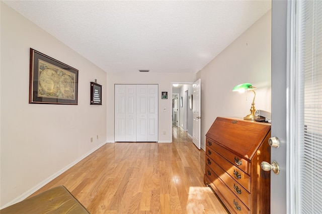 interior space with baseboards, light wood-type flooring, visible vents, and a textured ceiling