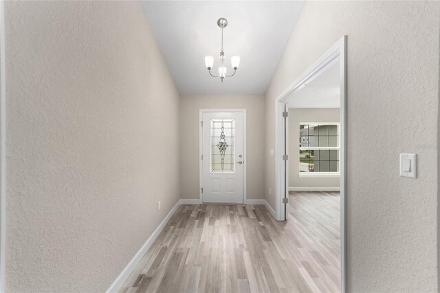 entrance foyer with vaulted ceiling, an inviting chandelier, a textured wall, baseboards, and light wood finished floors
