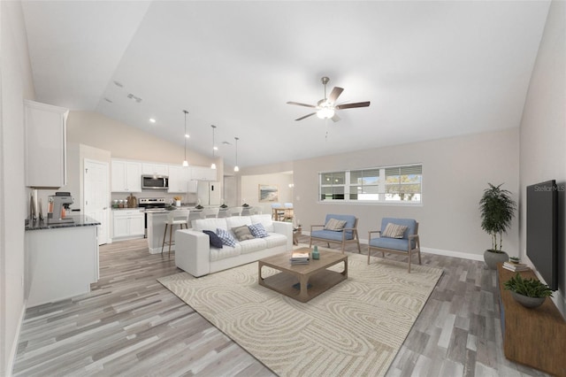 living area with baseboards, high vaulted ceiling, light wood-style flooring, and a ceiling fan