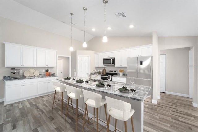 kitchen with a breakfast bar, an island with sink, visible vents, appliances with stainless steel finishes, and wood finished floors