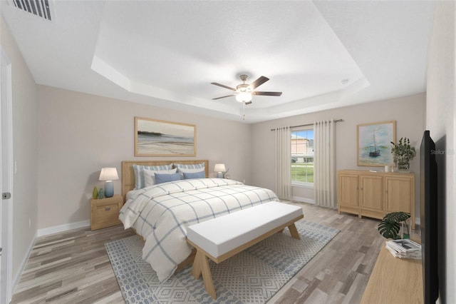 bedroom with visible vents, light wood finished floors, baseboards, a ceiling fan, and a tray ceiling