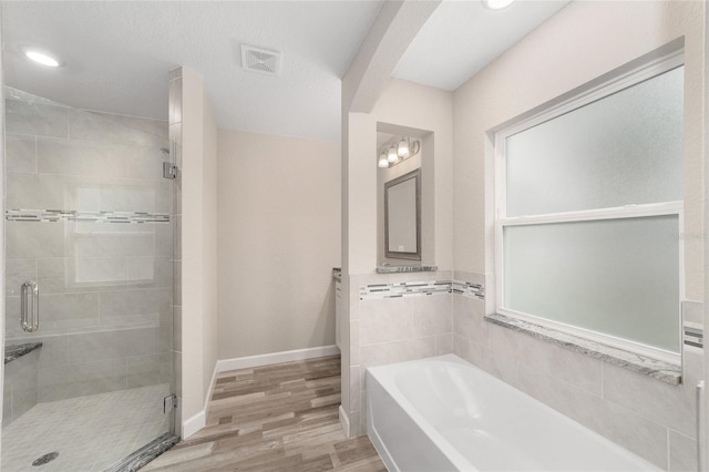 bathroom with a stall shower, wood finished floors, a bath, baseboards, and visible vents
