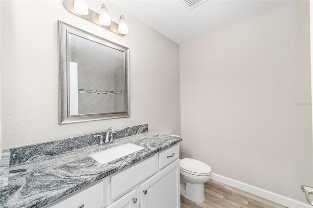 bathroom with toilet, vanity, wood finished floors, baseboards, and visible vents