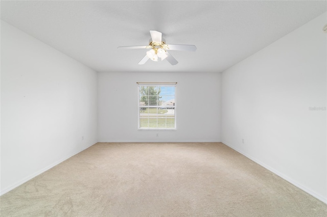spare room featuring light colored carpet, ceiling fan, and baseboards