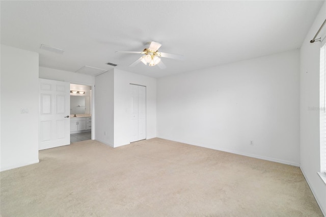 unfurnished bedroom featuring attic access, light colored carpet, ensuite bath, a ceiling fan, and a closet