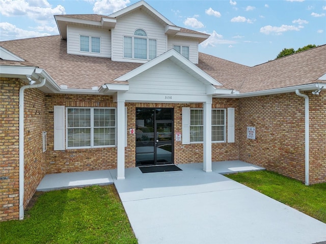 property entrance with a shingled roof and brick siding