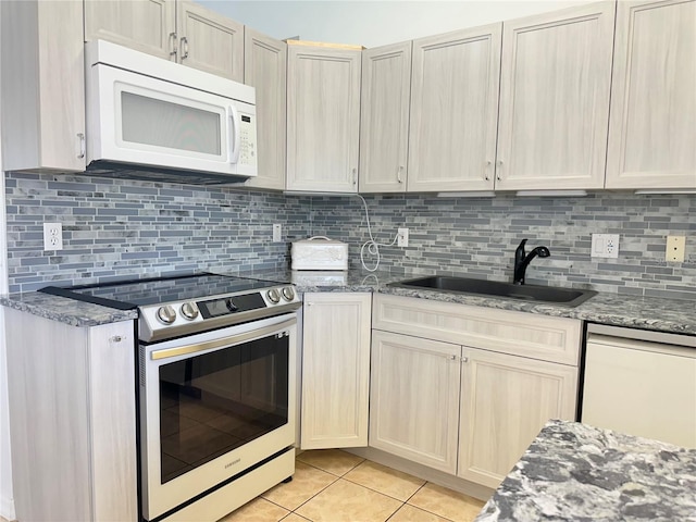 kitchen featuring light tile patterned floors, white appliances, stone countertops, and a sink