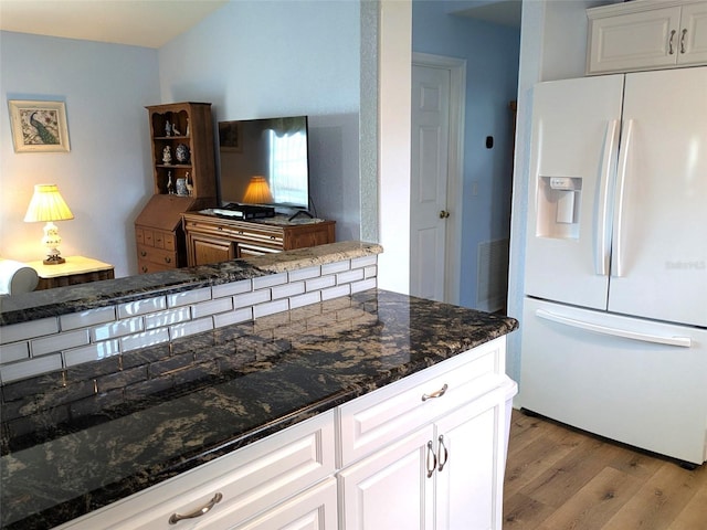 kitchen with light wood-style floors, dark stone counters, white fridge with ice dispenser, and white cabinetry