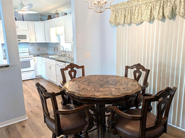 dining space with light wood-style floors, ceiling fan with notable chandelier, and baseboards